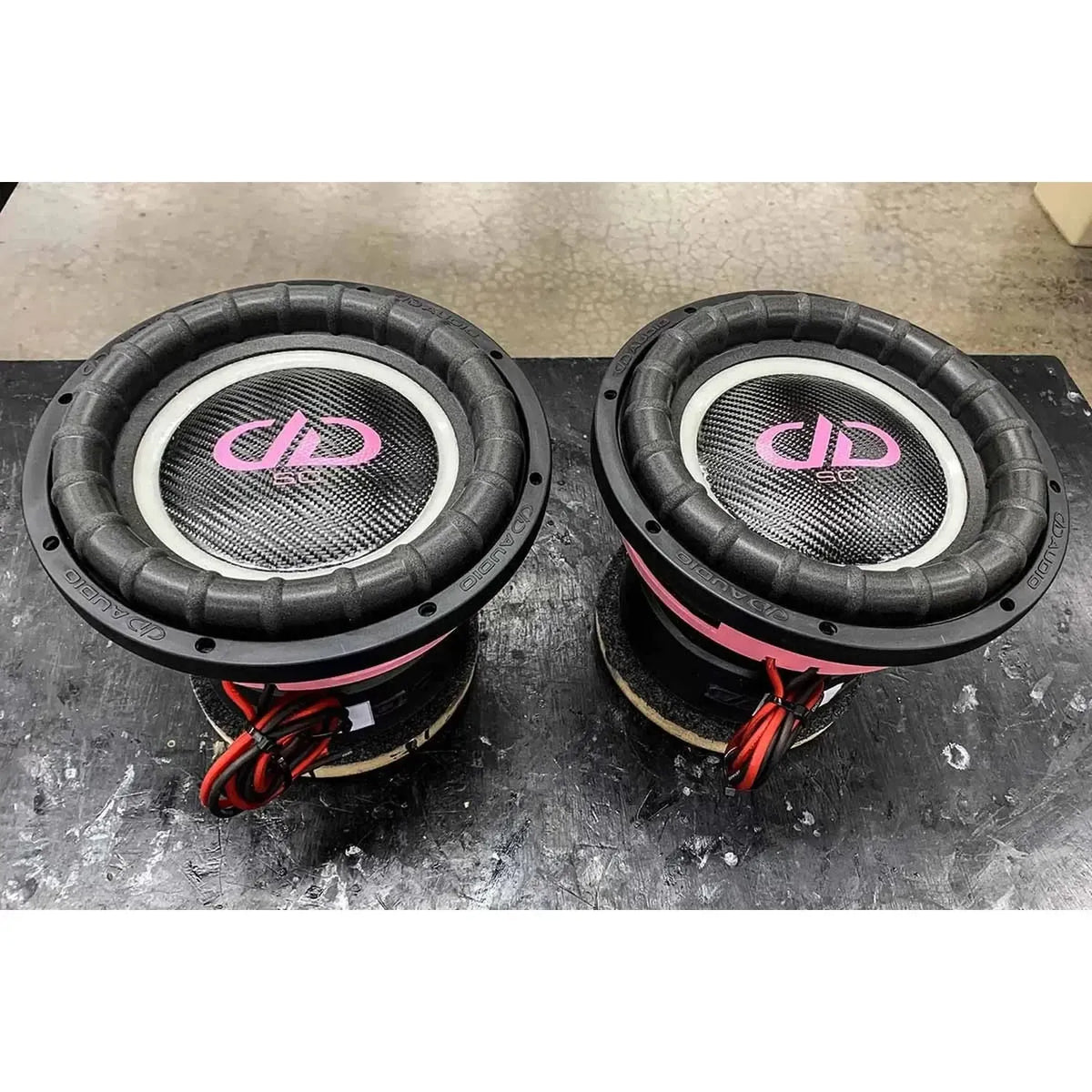 Two DD Audio Power Tuned 9512k ESP subwoofers with carbon fiber blend cones, red wires, and the DD logo sit on a black work surface.