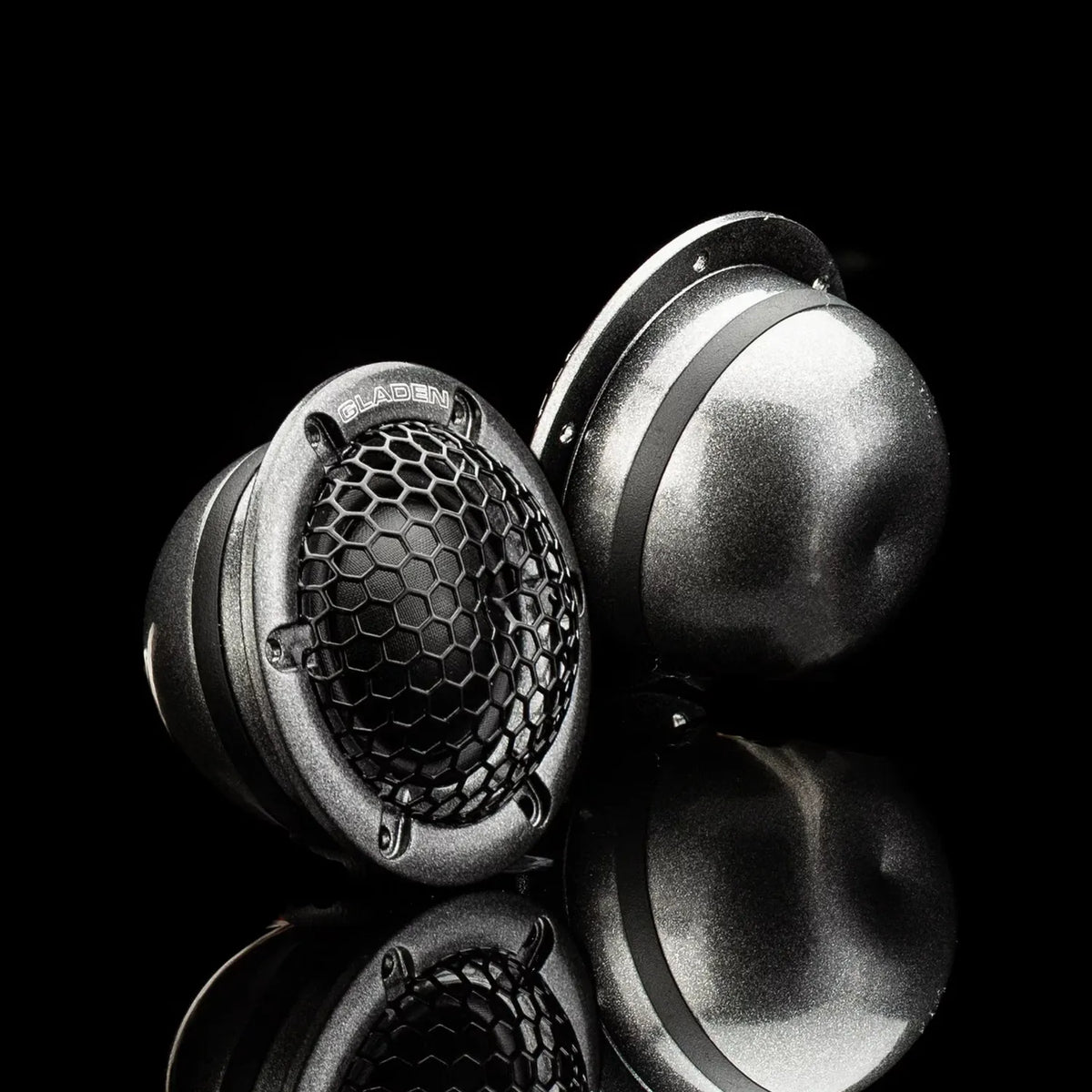 Deux tweeters à dôme métallique Gladen Aerospace 28, dont lun est doté dune grille en nid dabeille et dun logo, présentés sur une surface noire brillante.