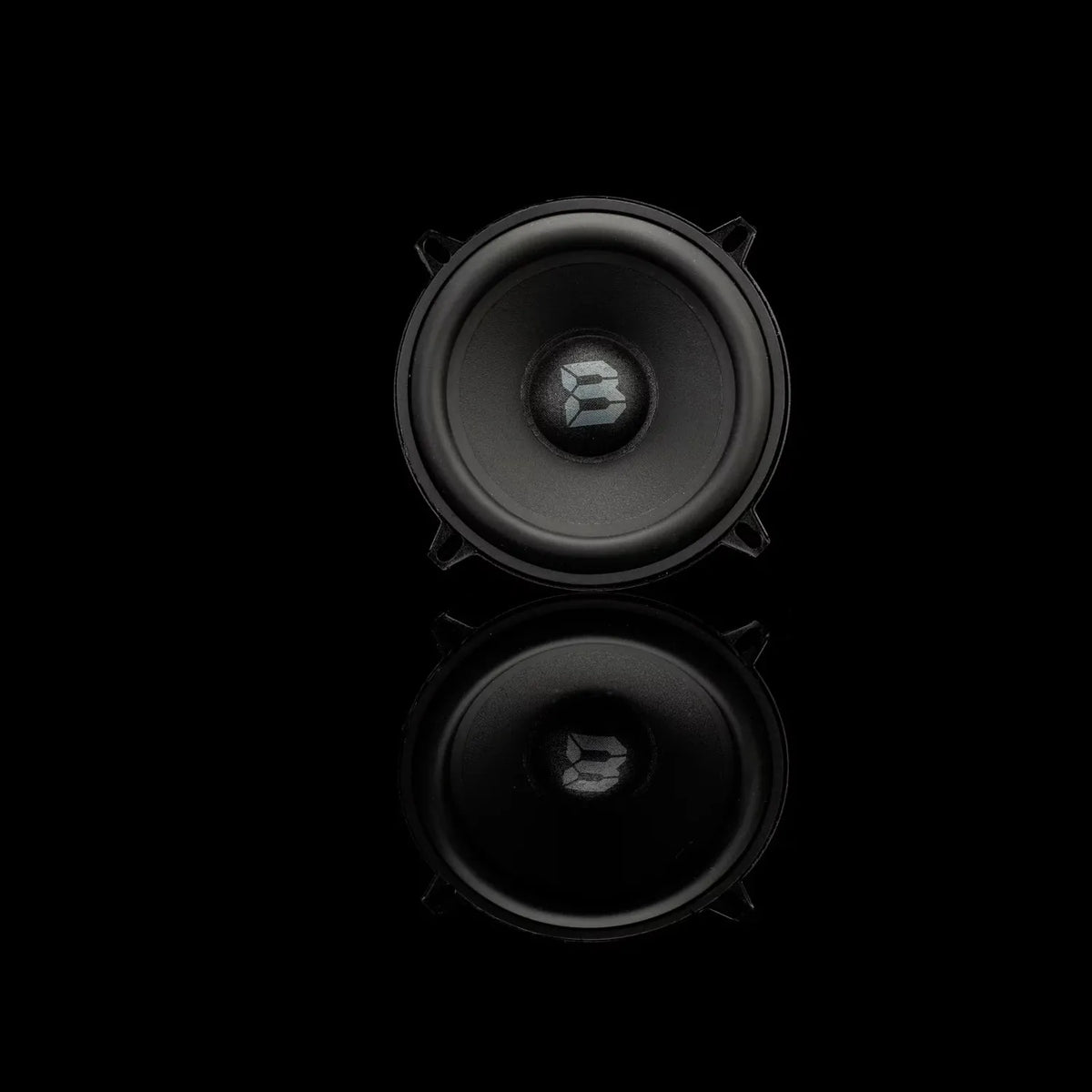 A Gladen Beta 130.2 speaker set is shown with a silver logo in the center, placed on a black background with its glossy reflection beneath.