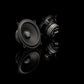 Two Gladen Beta 130.2 speakers are shown on a glossy black surface, highlighting the 2-Wege-Komponentensystem design with clear front and back reflections.