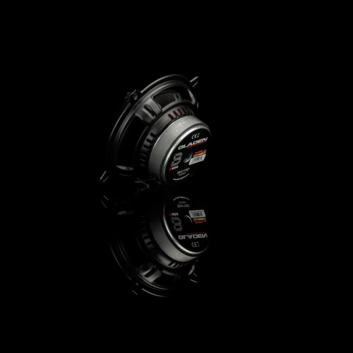 A compact black and silver Gladen Beta 130.2 is shown against a black background, its reflection visible below.