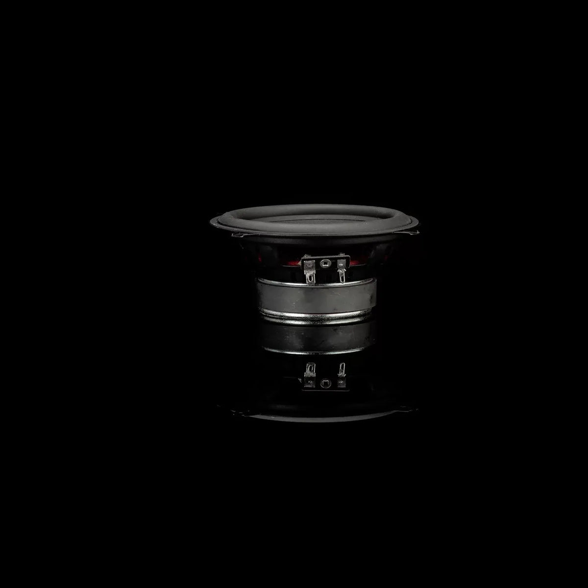 A Gladen Beta 130.2 speaker with a black cone and silver rim is centered on a black background, its reflection visible below.