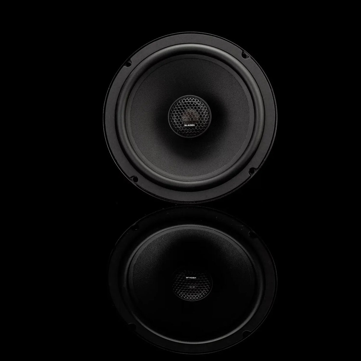 A black Gladen BETA 165-X speaker with a circular design is centered on a black background, showing its reflection below.