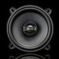A close-up of a Gladen Gamma 130-X speaker with a textured cone and four mounting holes, displayed against a black background.