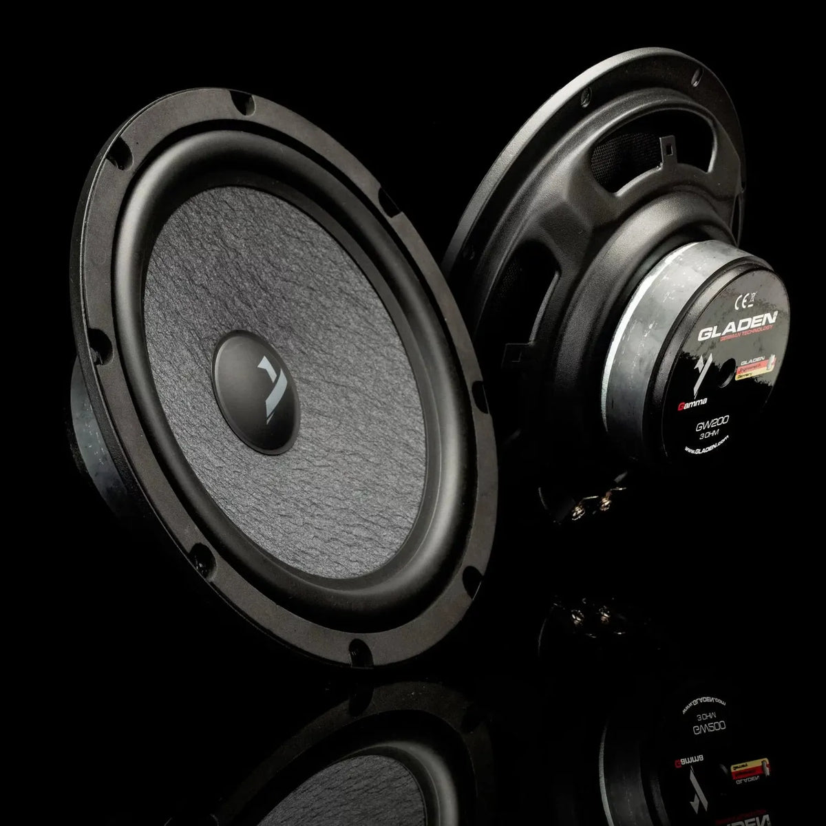 Two black Gladen Gamma 200.2 AC speakers, one front and one rear view, sit on a glossy surface with a dark background. Includes 8 Zoll Lautsprecherset.