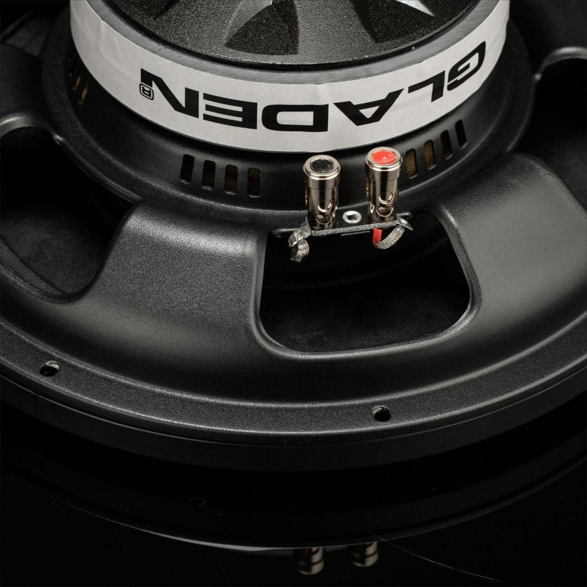 Close-up van de achterkant van de Gladen GS12-Slim-subwoofer, waarop het merklogo, de metalen aansluitingen en een deel van het zwarte 12-inch frame te zien zijn.