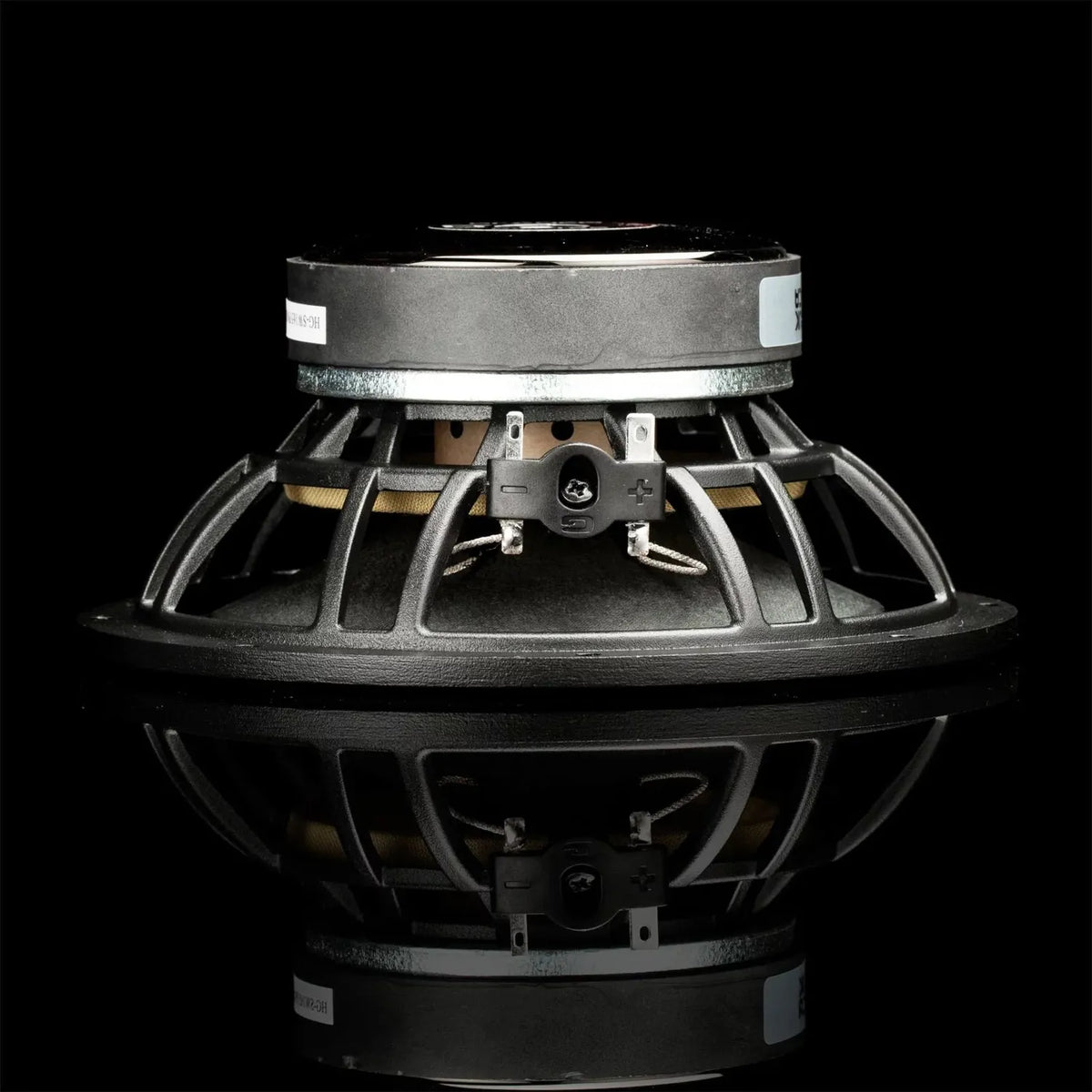On voit ici un haut-parleur dautoradio Gladen Sigma 165 avec cadre métallique, photographié de profil sur une surface noire brillante.