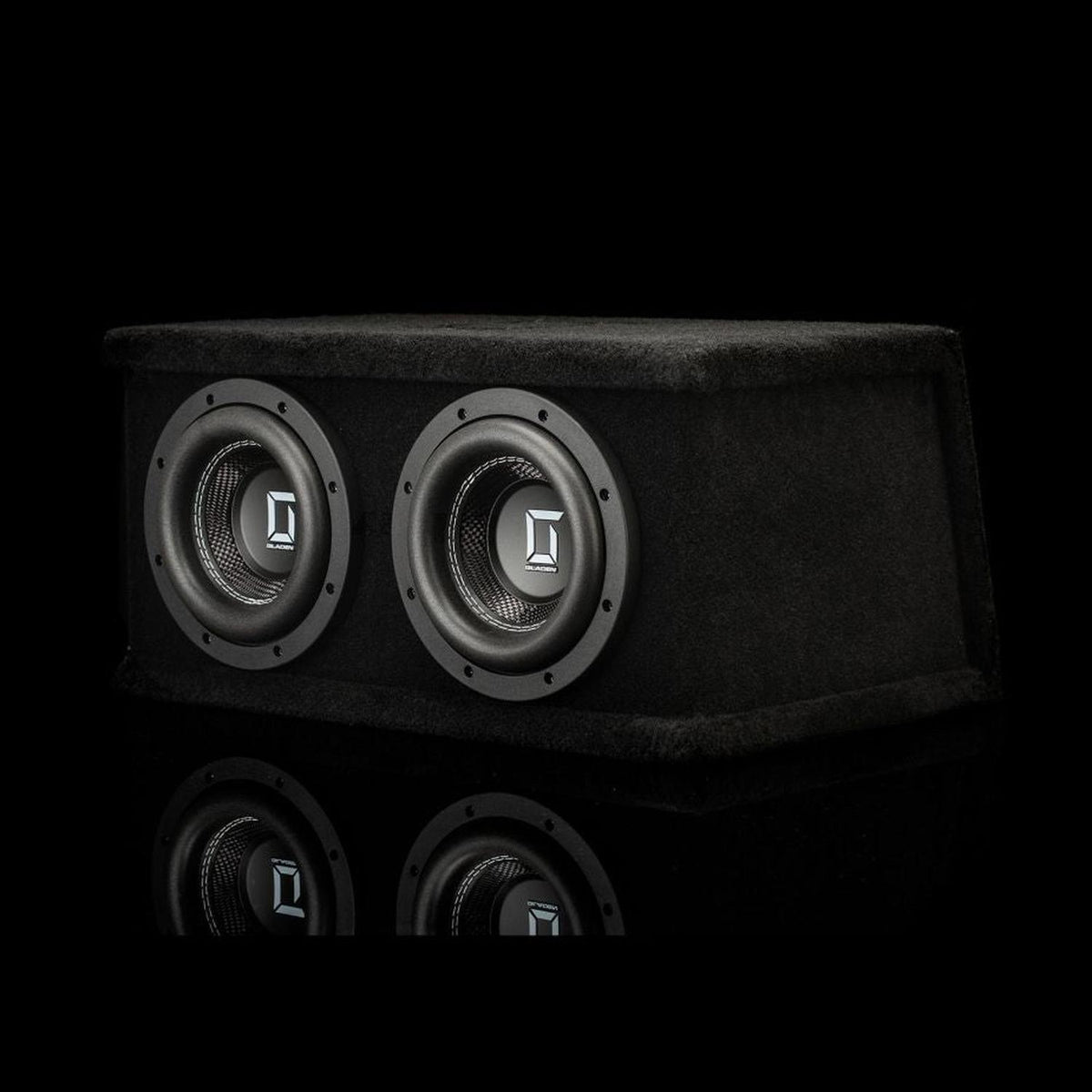 Il Gladen Sigma SSWX065 Dual è un subwoofer nero di forma rettangolare dotato di due driver da 6,5 pollici, raffigurato su uno sfondo nero sul quale si intravede il suo riflesso nella parte inferiore.