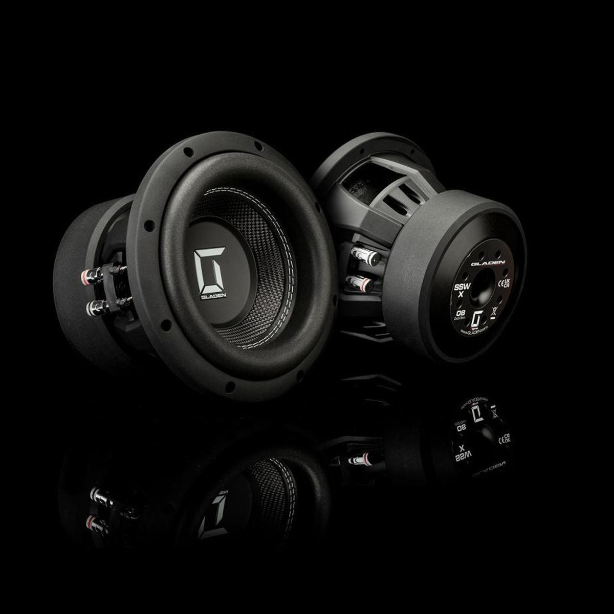 Deux subwoofers pour voiture Gladen Sigma SSWX08 sont présentés sur une surface noire réfléchissante, avec le logo bien visible : lun est orienté vers lavant et lautre montre son dos.