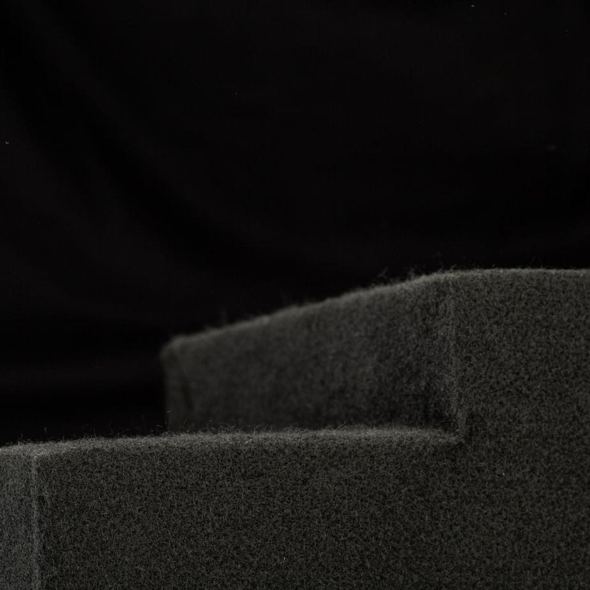 A close-up of dark gray foam with a stepped edge, showcasing Gladens Subbox-Buz.2 for the VW ID.Buzz subwoofer against a black background.