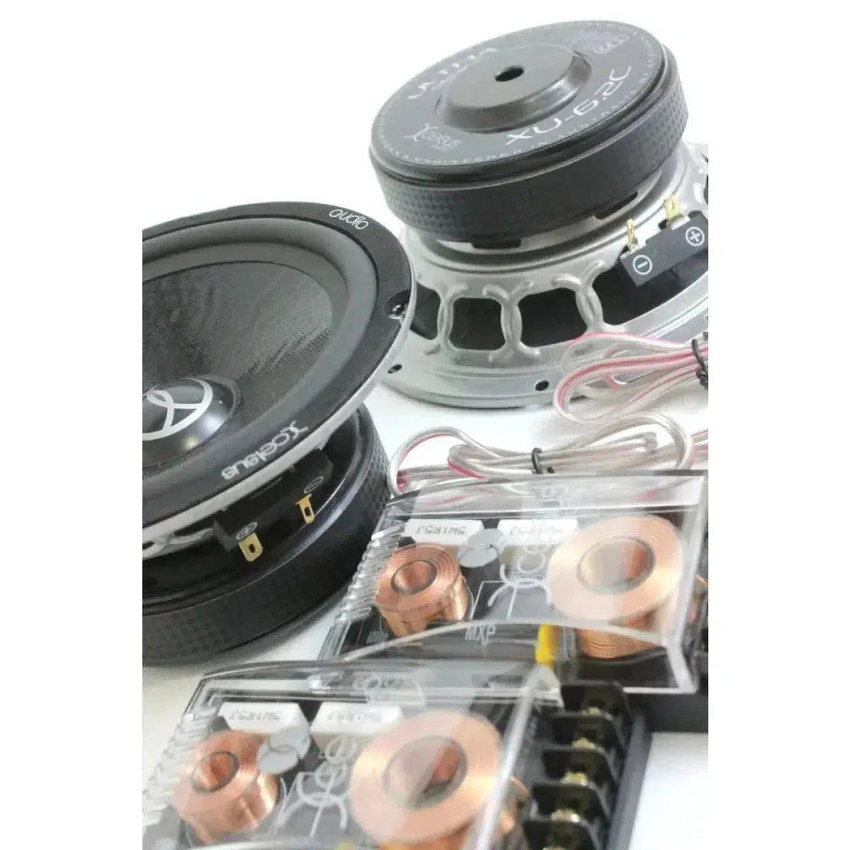 Se muestran dos altavoces de coche Xcelsus Ultra XU6.2C de 6 pulgadas en negro y dos unidades de cruce con bobinas de cobre expuestas sobre una superficie blanca.
